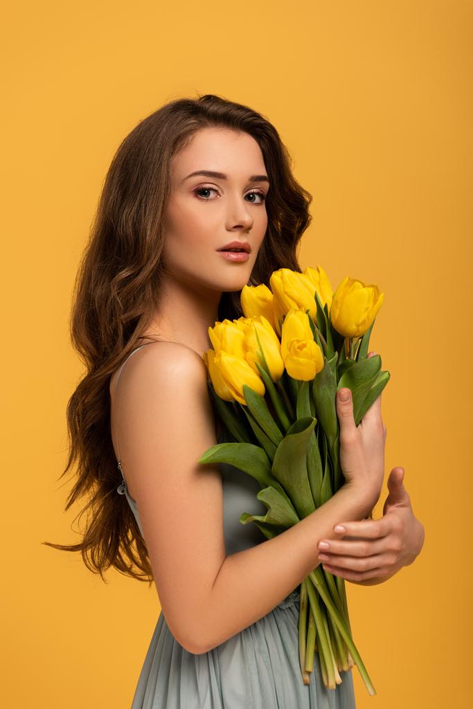 mulher atraente em vestido de primavera segurando buquê de flores de tulipa isolado no amarelo
 - Foto, Imagem