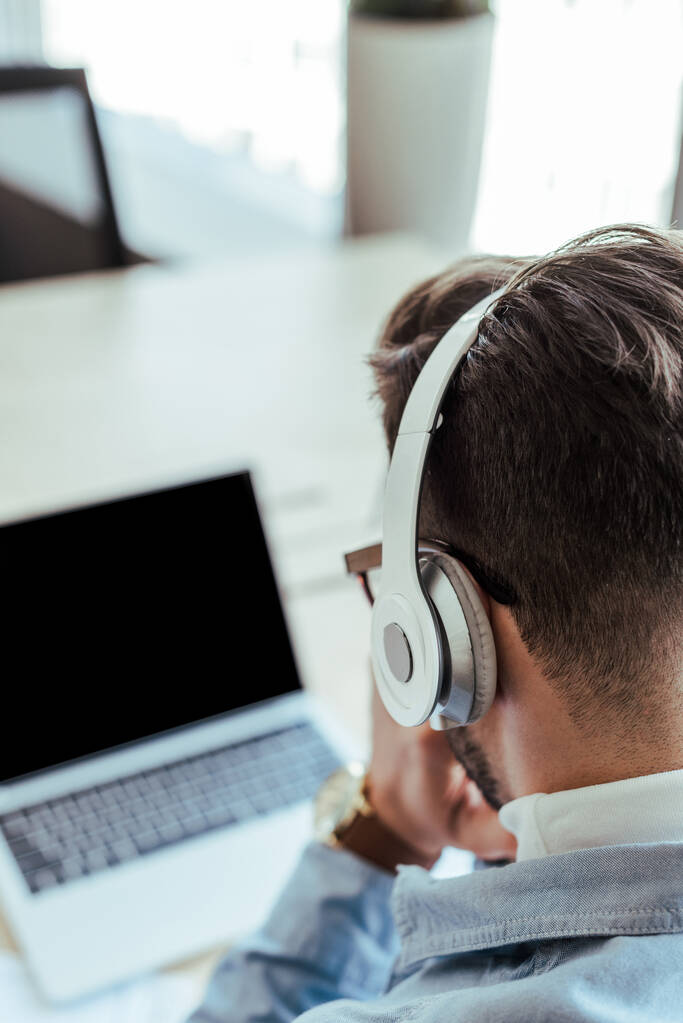 Selective focus of IT worker in headphones with laptop in coworking space - Photo, Image