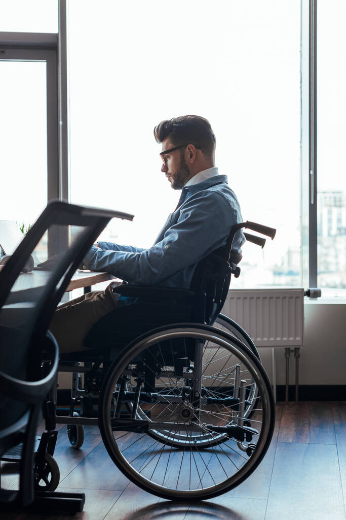 Enfoque selectivo del trabajador de TI con discapacidad concentrada en silla de ruedas que trabaja en un espacio de coworking
 - Foto, Imagen
