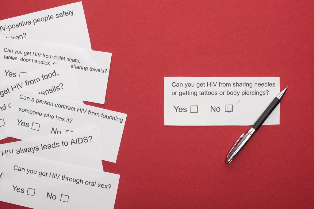 πάνω όψη χάρτινων καρτών με ερωτηματολόγιο για τον HIV και πένα σε κόκκινο φόντο - Φωτογραφία, εικόνα