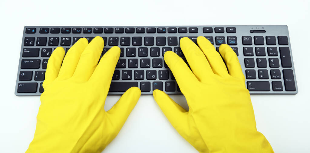 A man in bright yellow rubber gloves is typing on the keyboard. Disinfection in public places, the fight against the virus, coronavirus. - Photo, Image