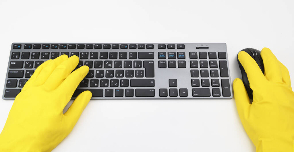 Een man met felgele rubberen handschoenen typt op het toetsenbord. Desinfectie op openbare plaatsen, bestrijding van het virus, coronavirus. - Foto, afbeelding