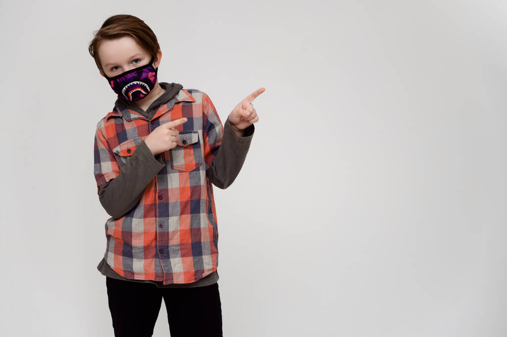 Foto van een gemaskerde jongen in een geruit shirt op een witte achtergrond toont zijn handen naar de zijkanten - Foto, afbeelding