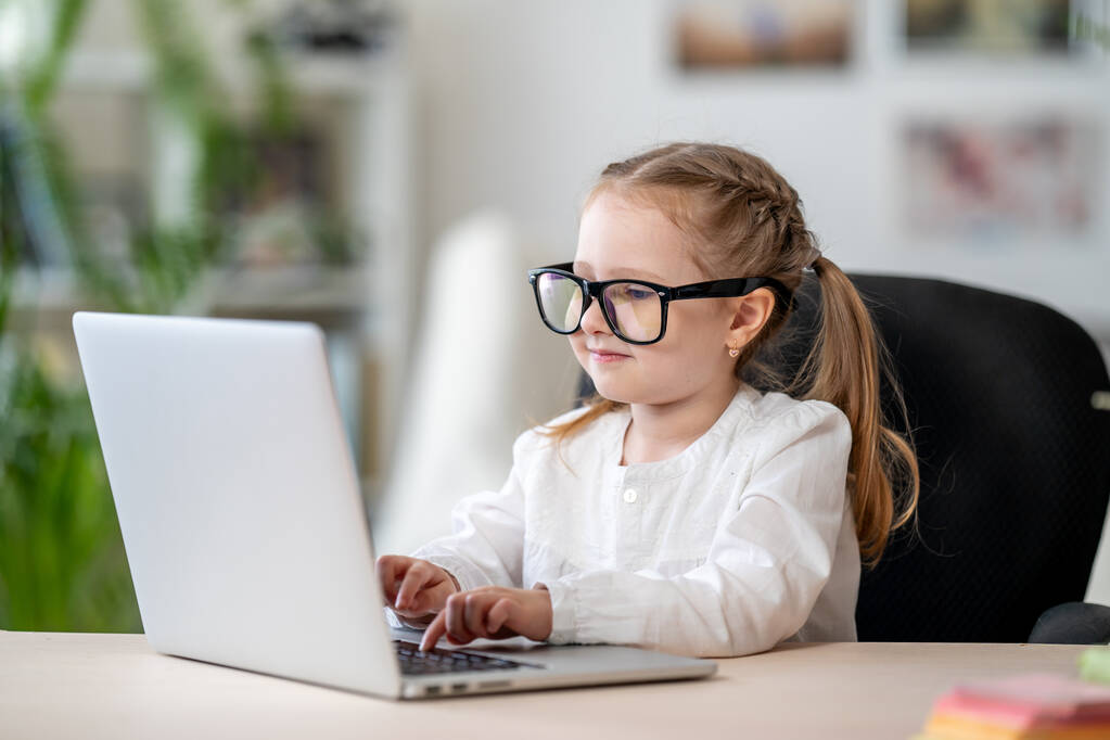 Söpö pieni tyttö, jolla on lasit kannettavan digitaalisen e-oppimisen konseptin avulla karanteenin ja itseeristyksen aikana. Covid-19-koronavirus-pandemian aiheuttama etäopiskelu
 . - Valokuva, kuva
