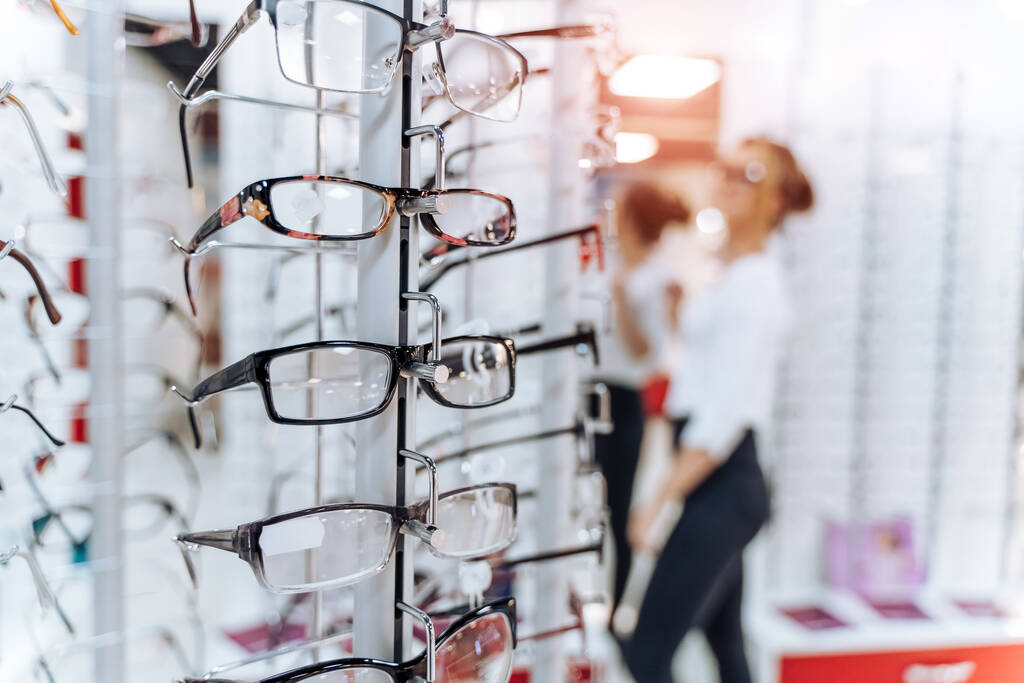 Fila de gafas en una óptica. Tienda de anteojos. Soporte con gafas en la tienda de óptica. La mujer elige los anteojos. Corrección de la vista. - Foto, Imagen