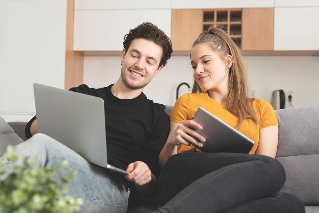 Para korzystająca z szybkiego Internetu domowego z laptopem i tabletem cyfrowym. Kobieta i mężczyzna na kanapie w salonie - Zdjęcie, obraz