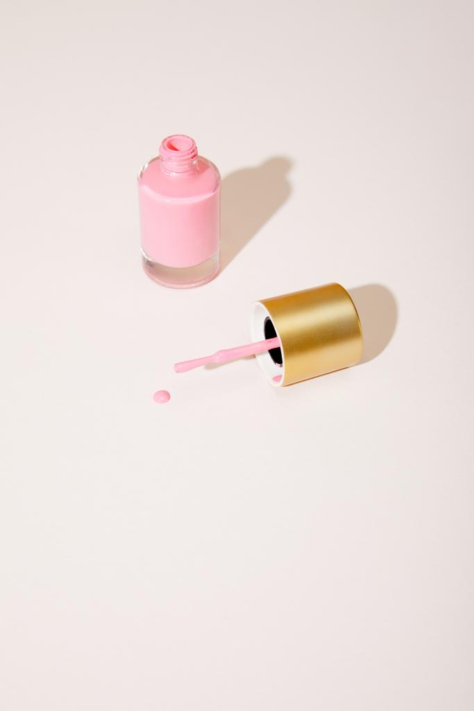 Высокоугольный вид открытой бутылки розового лака для ногтей на белом фоне
 - Фото, изображение