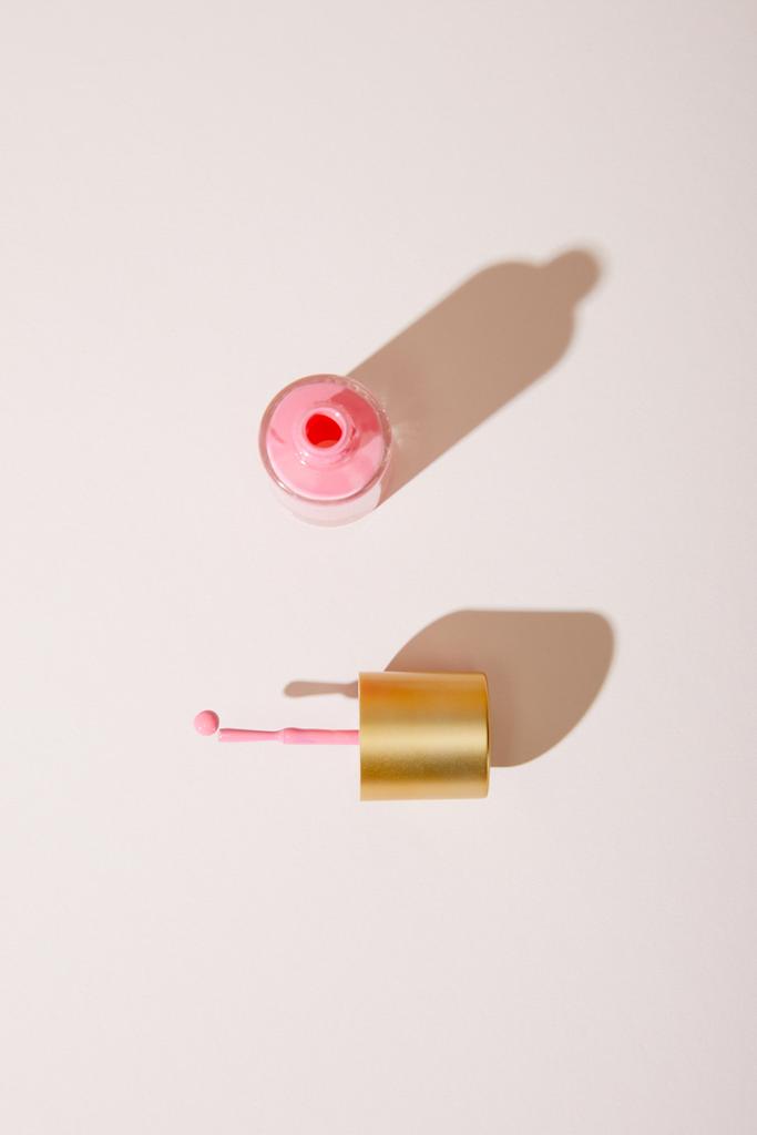 Κάτοψη του ανοιγμένου μπουκαλιού από ροζ βερνίκι νυχιών σε λευκό φόντο - Φωτογραφία, εικόνα