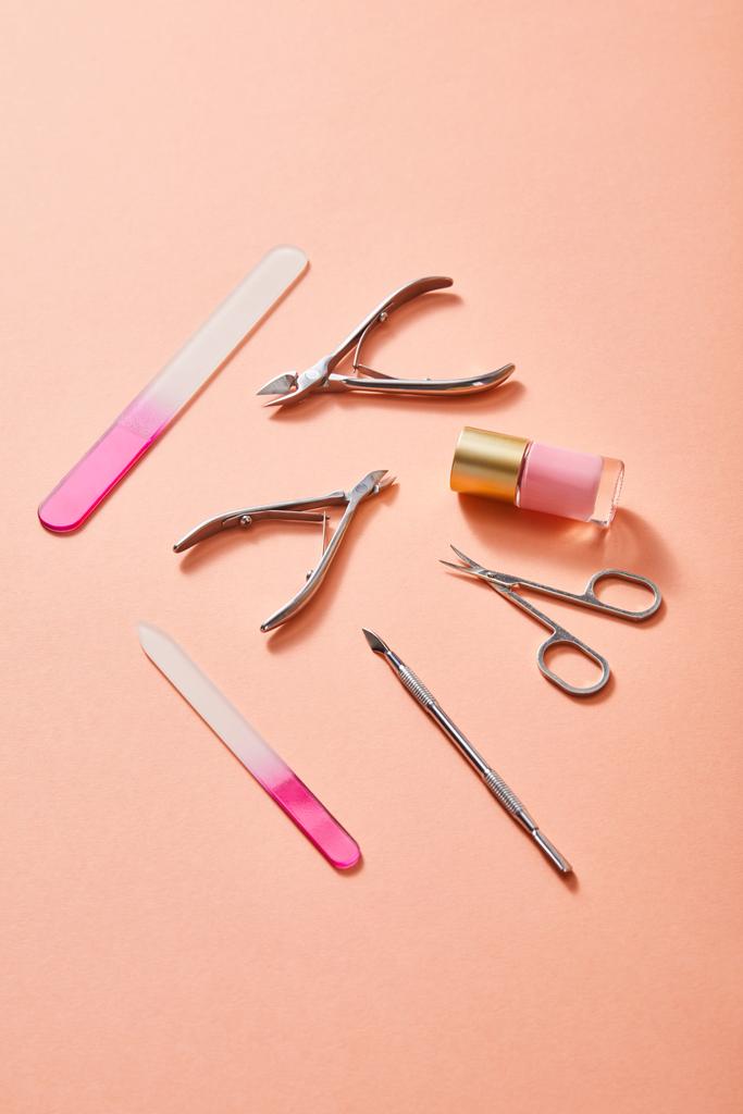 High angle view of bottle of pink nail polish and manicure instruments on coral background - Photo, Image