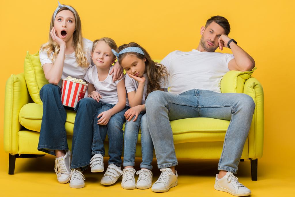 βαριεστημένοι γονείς και παιδιά βλέπουν ταινία στον καναπέ με τον κουβά ποπ κορν στο κίτρινο  - Φωτογραφία, εικόνα