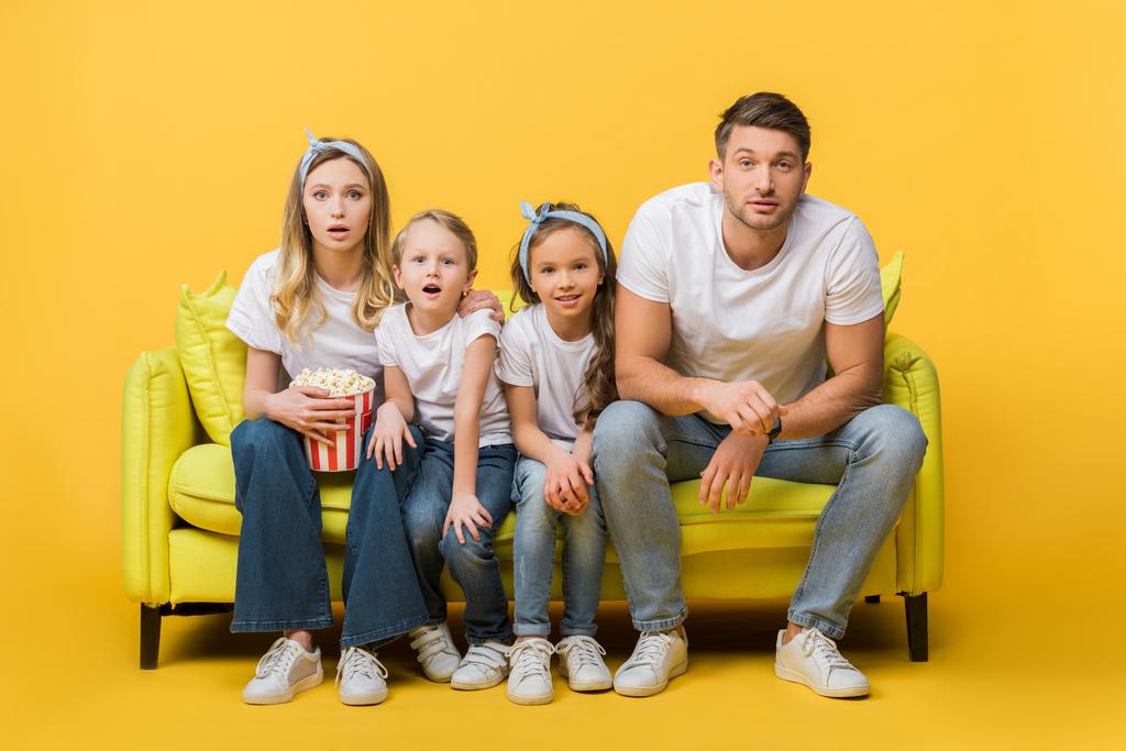 έκπληκτη οικογένεια βλέποντας ταινία στον καναπέ με τον κουβά ποπ κορν στο κίτρινο  - Φωτογραφία, εικόνα