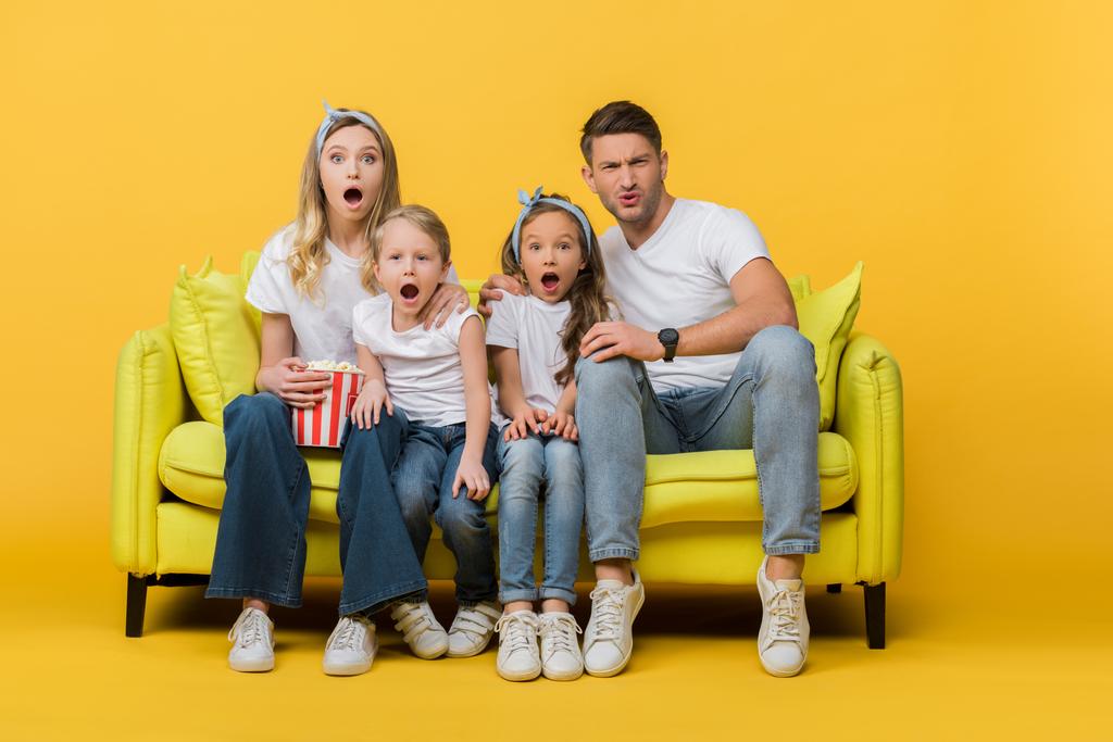 σοκαρισμένη οικογένεια βλέποντας ταινία στον καναπέ με τον κουβά ποπ κορν στο κίτρινο  - Φωτογραφία, εικόνα