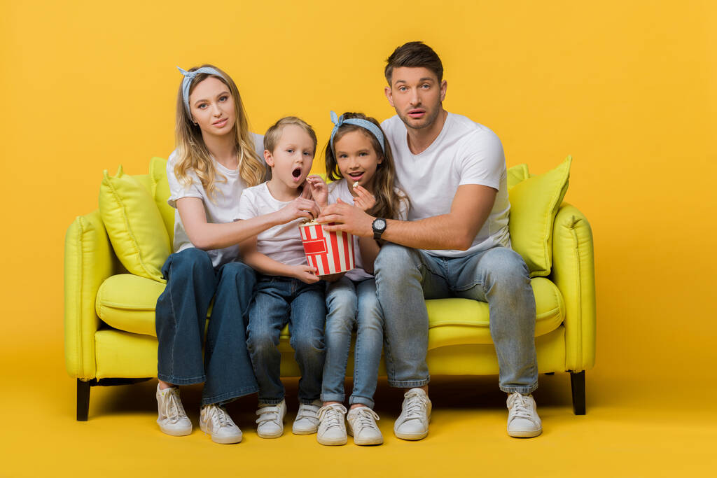 překvapená rodina sledování filmu na pohovce s popcorn vědro na žluté  - Fotografie, Obrázek