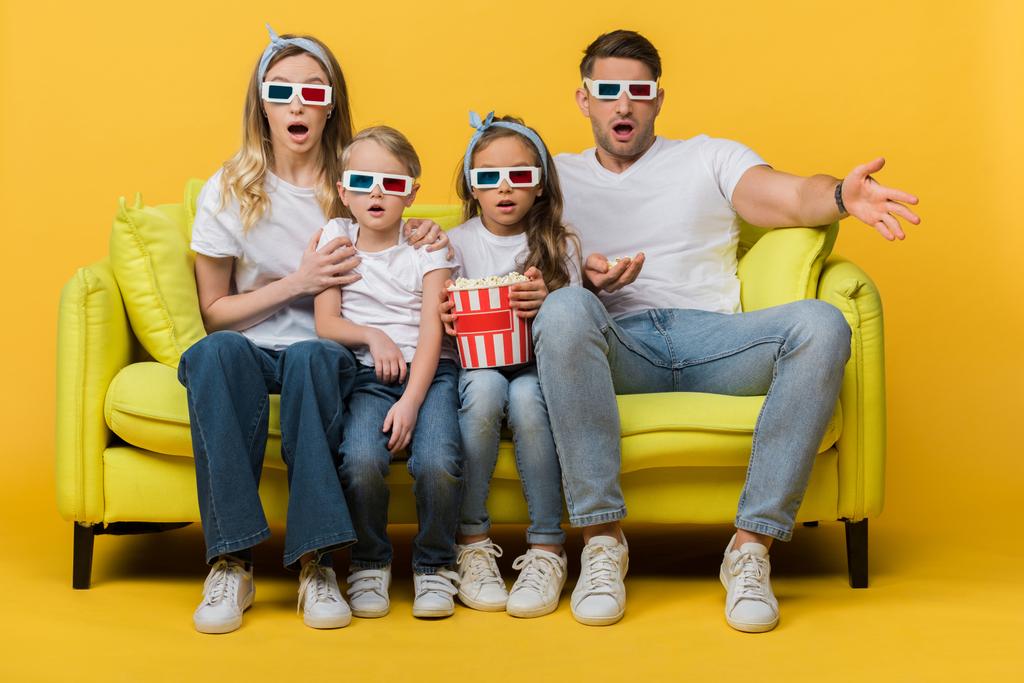 σοκαρισμένη οικογένεια σε 3D γυαλιά βλέποντας ταινία στον καναπέ με τον κουβά ποπ κορν στο κίτρινο  - Φωτογραφία, εικόνα