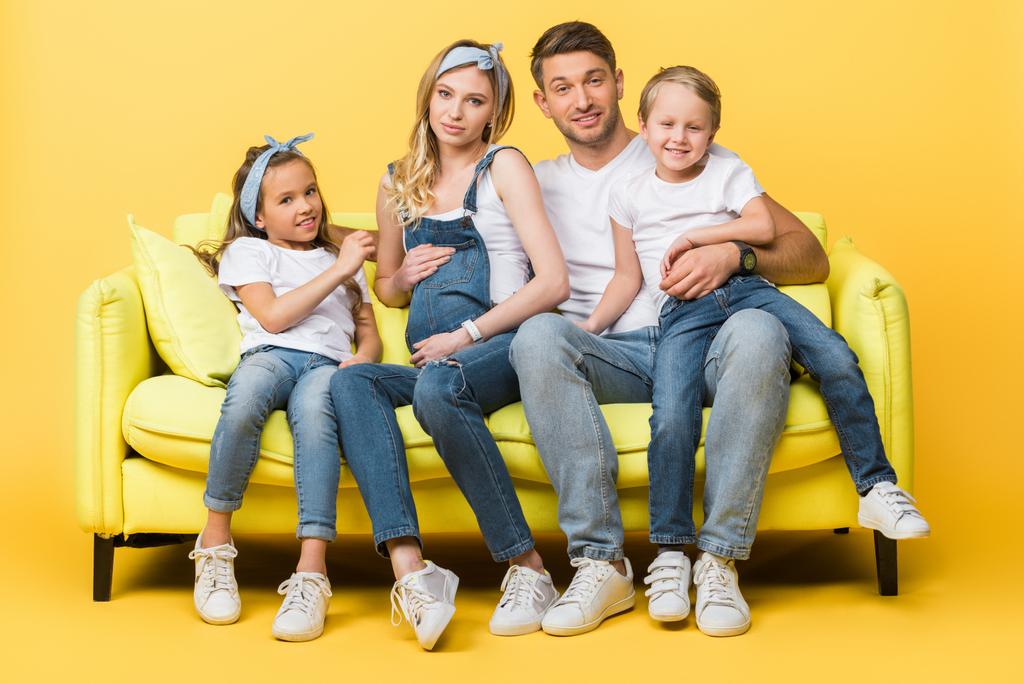 happy pregnant mother, father and children sitting on sofa on yellow   - Photo, Image