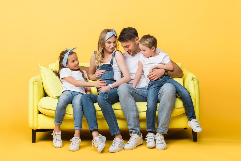 emotional pregnant wife, husband and children sitting on sofa on yellow   - Photo, Image