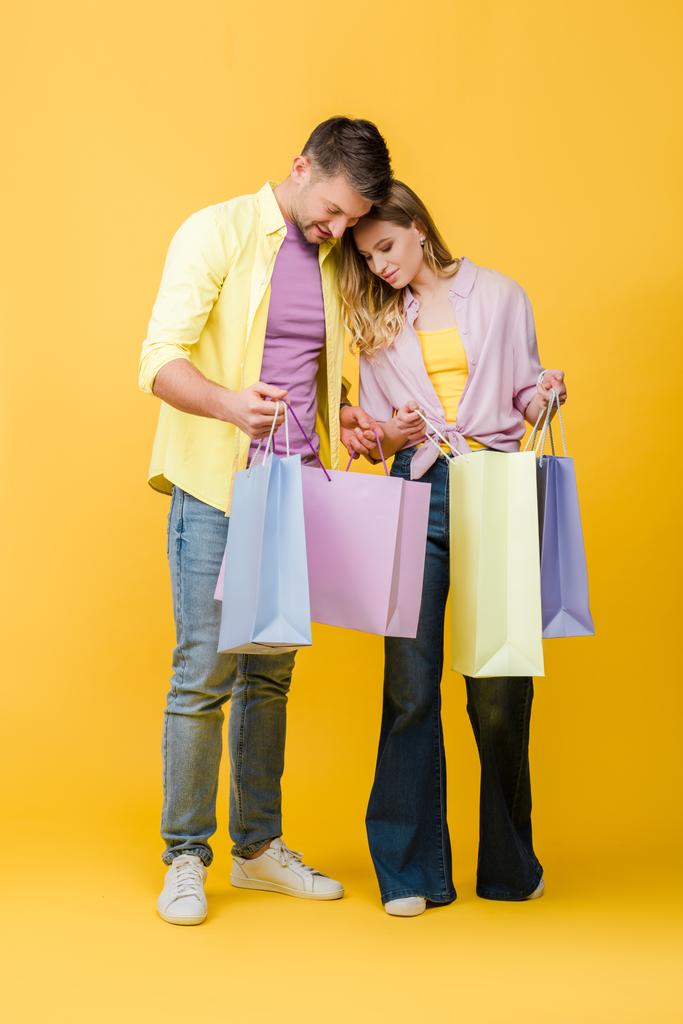 hermosa pareja feliz mirando en bolsas de compras en amarillo
 - Foto, Imagen
