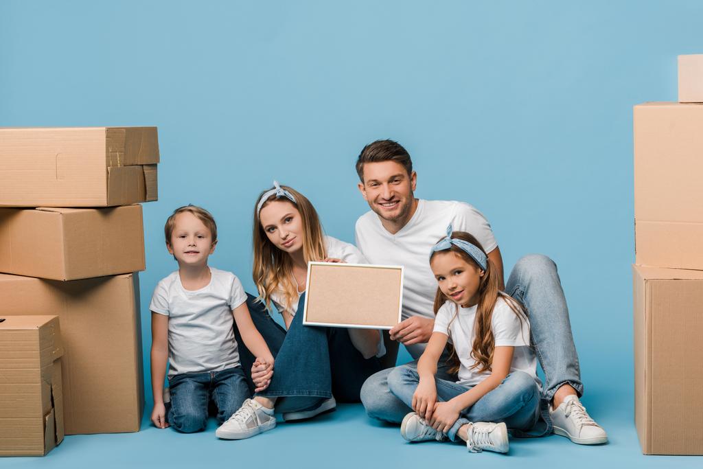 щасливі батьки і діти тримають рамку і сидять на синьому з картонними коробками для переміщення
 - Фото, зображення