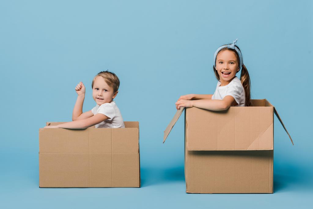 adoráveis irmãos alegres brincando em caixas de papelão em azul
 - Foto, Imagem