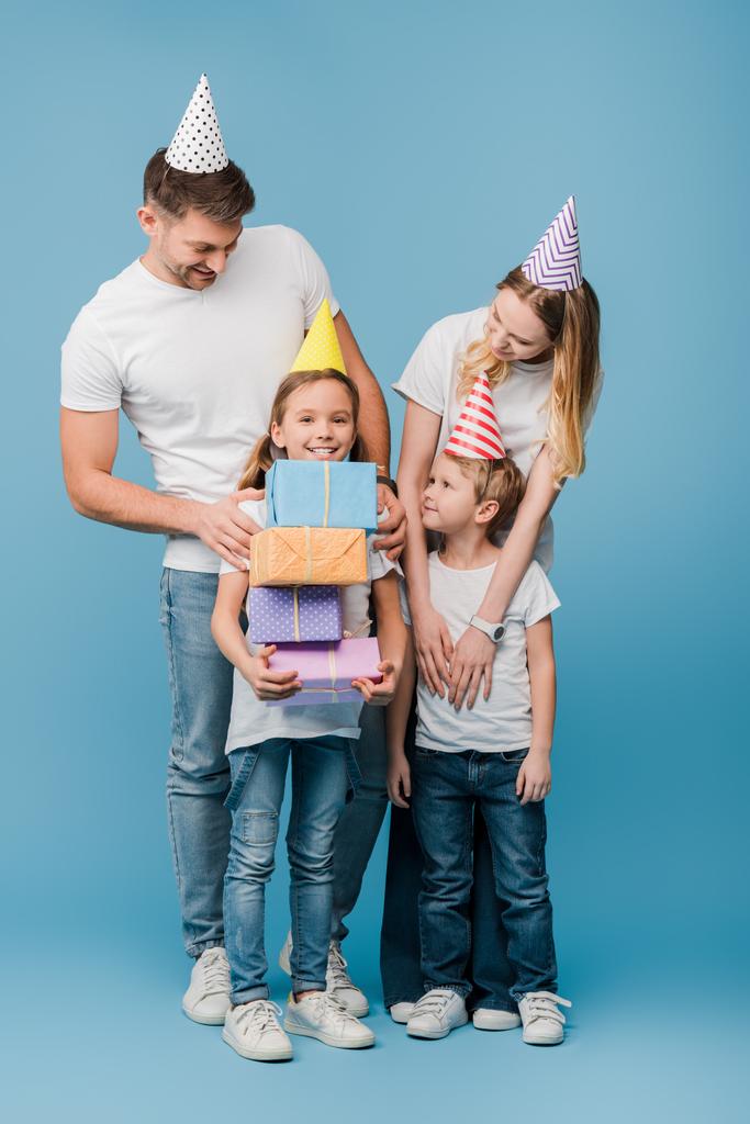 glückliche Familie in Geburtstagskappen, Tochter hält Geschenkboxen auf blau - Foto, Bild