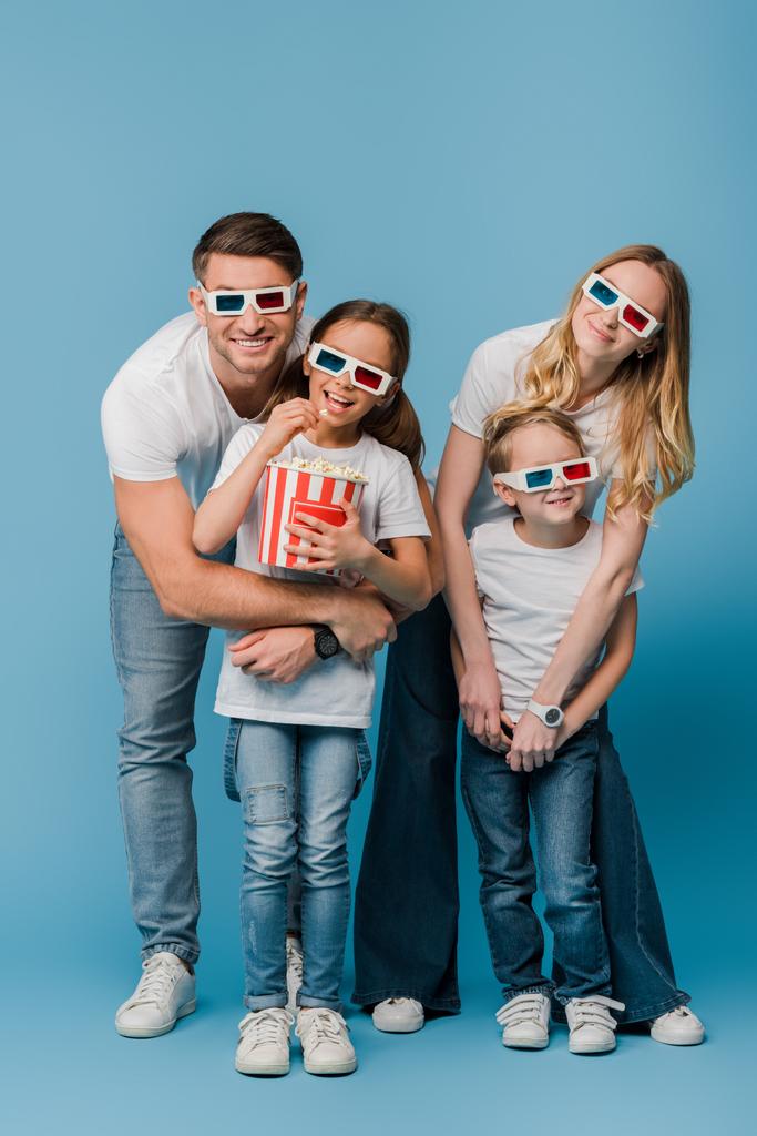 Mutlu ebeveynler ve çocuklar 3 boyutlu gözlüklerle film izliyor ve mavi üzerinde patlamış mısır kovası tutuyorlar. - Fotoğraf, Görsel