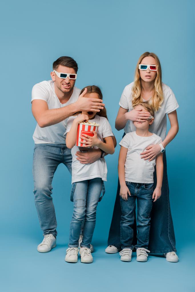 šokovaní rodiče ve 3D brýlích zavírající oči pro děti držící popcorn kbelík na modré - Fotografie, Obrázek