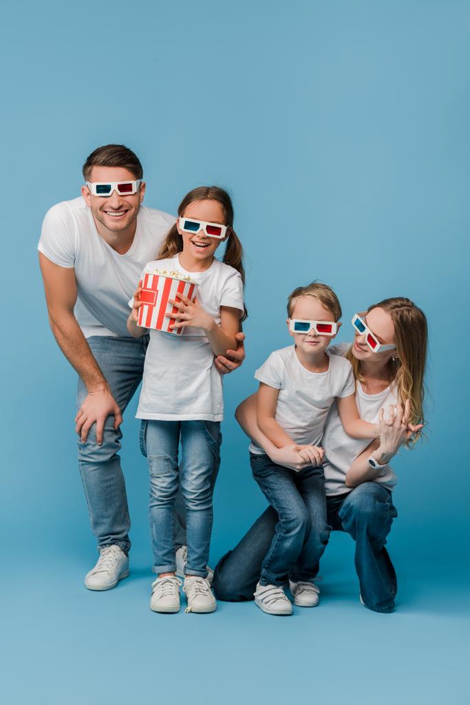 Счастливая семья смотрит фильм в 3D-очках и держит в руках кукурузное масло на голубом фоне
 - Фото, изображение