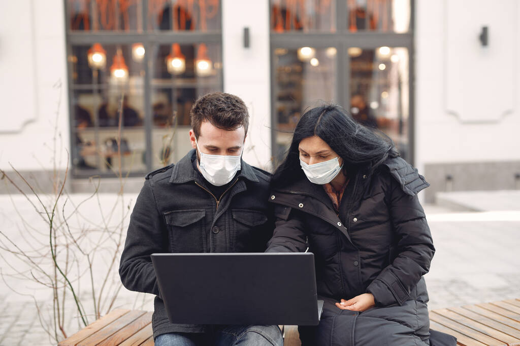 Maskierte sitzen mit Laptop in einer Stadt - Foto, Bild