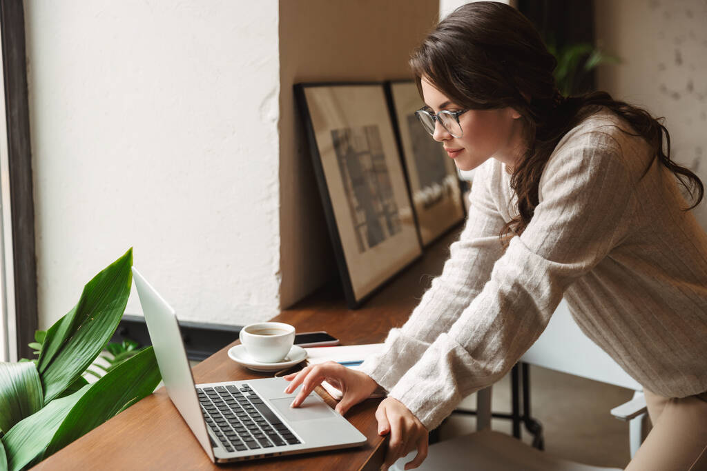 Imagem da jovem mulher branca bonita usando óculos usando laptop enquanto estudava no café
 - Foto, Imagem