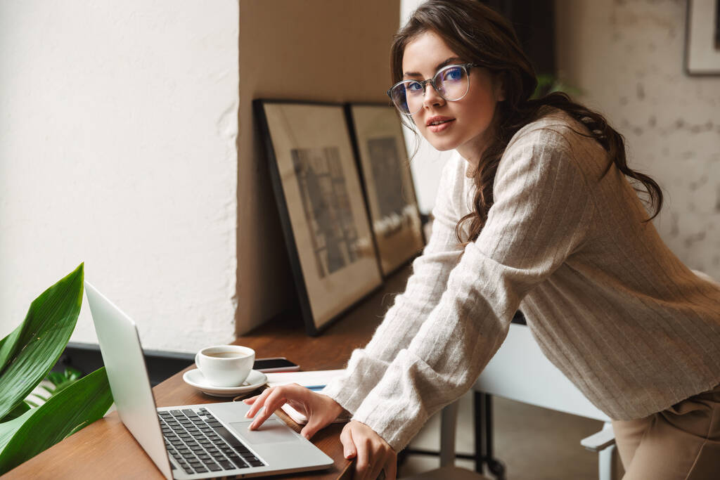 Immagine di una giovane donna caucasica che indossa occhiali da vista usando il computer portatile mentre studia nel caffè
 - Foto, immagini
