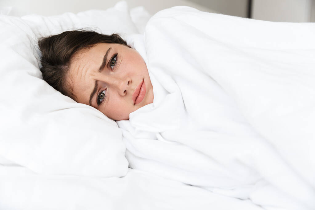 Sconvolto bella ragazza sdraiata a letto in camera da letto, che copre con coperta
 - Foto, immagini