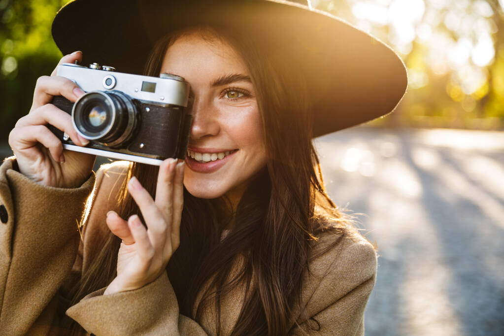 Kuva viettelevä nainen hattu hymyillen ottaessaan valokuvan retro kamera ulkona
 - Valokuva, kuva
