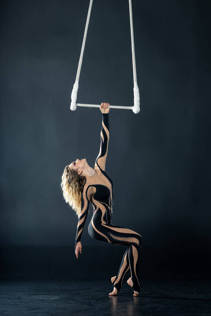 Una joven realiza los elementos acrobáticos en el trapecio de aire. Estudio de rodaje actuaciones sobre un fondo negro
 - Foto, Imagen