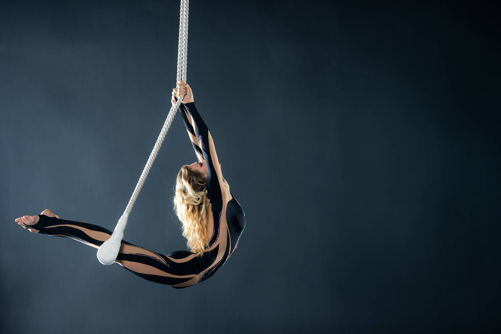 Nuori tyttö suorittaa akrobaattisia elementtejä ilmassa trapetsi. Studio ammunta esityksiä mustalla taustalla
 - Valokuva, kuva