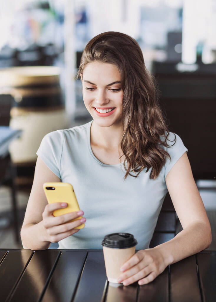 Jonge mooie vrouw met behulp van smartphone in cafe  - Foto, afbeelding