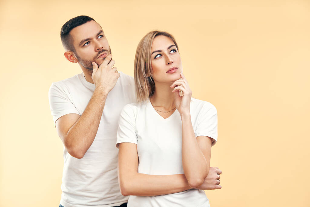 Young thoughtful man and woman looking sideways isolated on beige background. Doubt, interest concept - Photo, Image