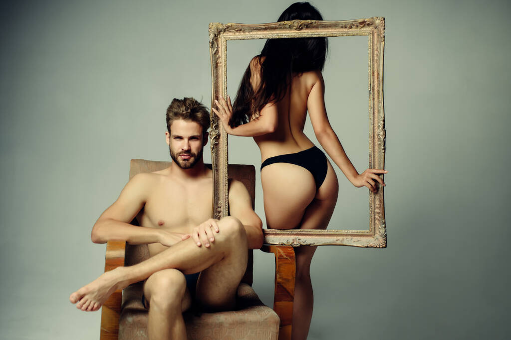 Beautiful sexy couple. Young woman holding an empty frame. Brunette girl in a black panties with guy with naked torso. Confident brutal man. Isolated gray background. - Photo, Image