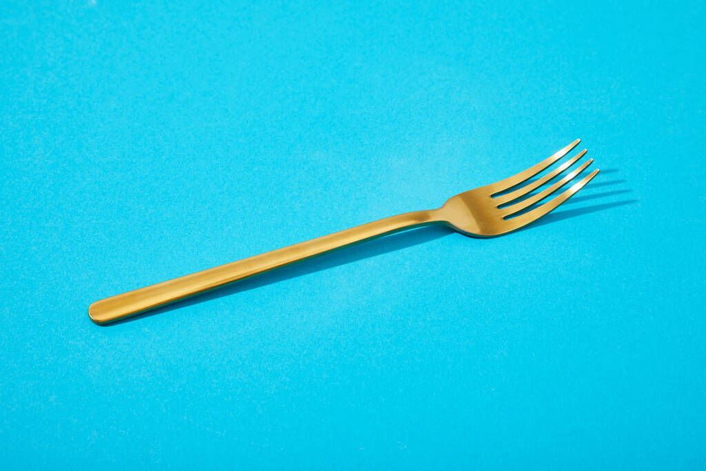 metalli kiiltävä kultainen haarukka sinisellä pohjalla
 - Valokuva, kuva
