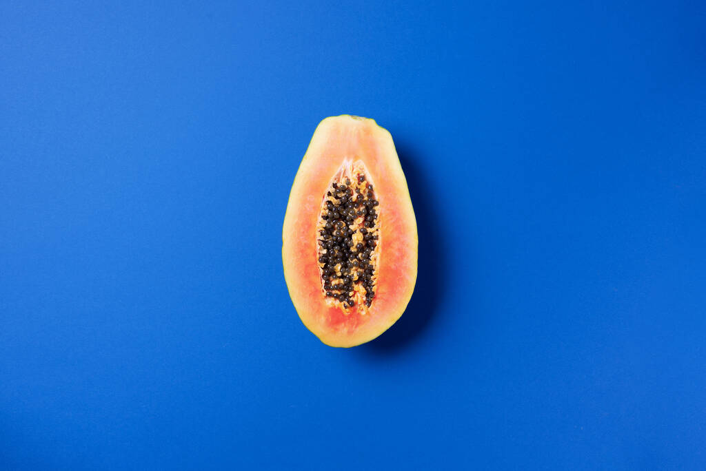 Halved papaya on blue background. Top view. Copy space. Summer time. Tropical travel, exotic fruit. Vegan and vegetarian concept - Photo, Image