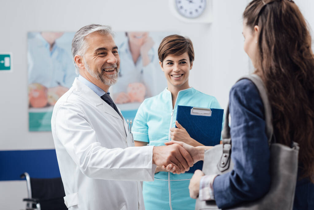 Orvosi személyzet fogadja a beteget a klinikán: az orvos ad egy kézfogás és mosolygós, orvosi szolgálat és egészségügyi szakemberek koncepció - Fotó, kép