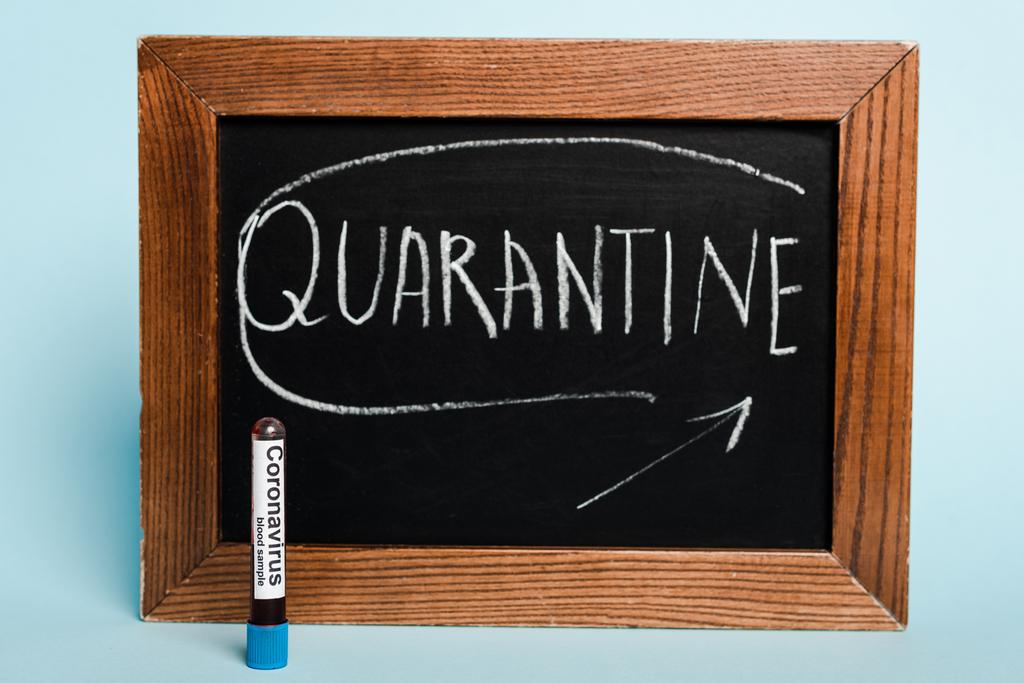 quarantaine-opschriften op schoolbord in de buurt van een reageerbuis met coronavirus-bloedmonster op blauwe achtergrond - Foto, afbeelding