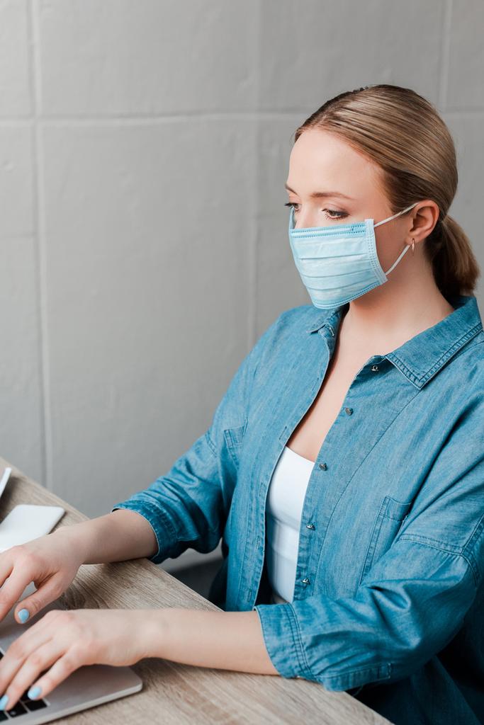 жінка в медичній масці працює з ноутбуком в офісі
 - Фото, зображення
