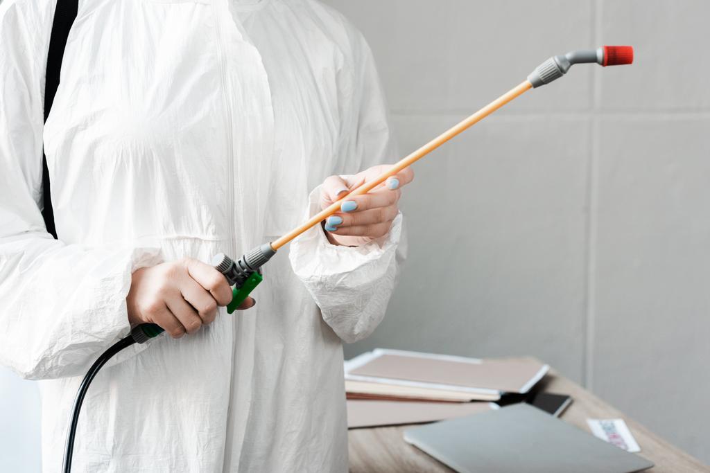 bijgesneden beeld van persoon in wit hazmat pak met desinfectie op kantoor, coronavirus concept - Foto, afbeelding