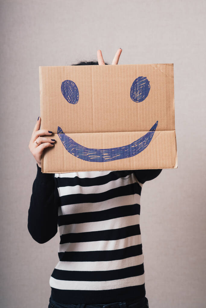 Vrouw met bruine kartonnen smiley. Grijze achtergrond - Foto, afbeelding