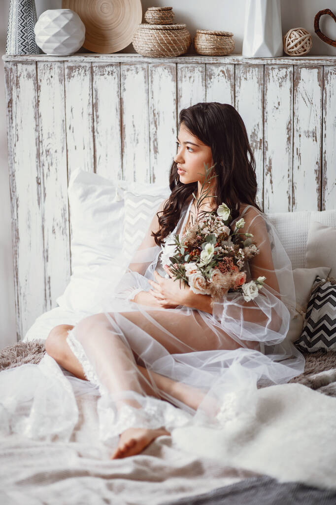 Asiatische Braut in Unterwäsche mit Brautstrauß auf dem Bett - Foto, Bild