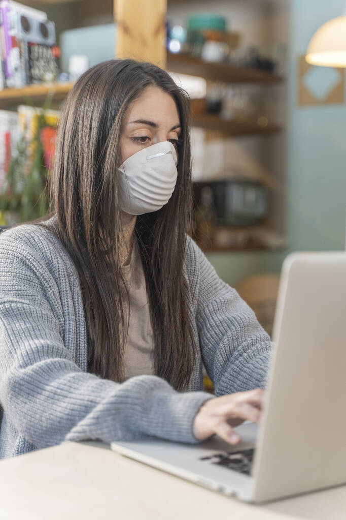 Coronavirus. Business woman working from home wearing protective mask. Business woman in quarantine for coronavirus wearing protective mask. Working from home.  Cleaning her hands with sanitizer gel.  - Photo, Image