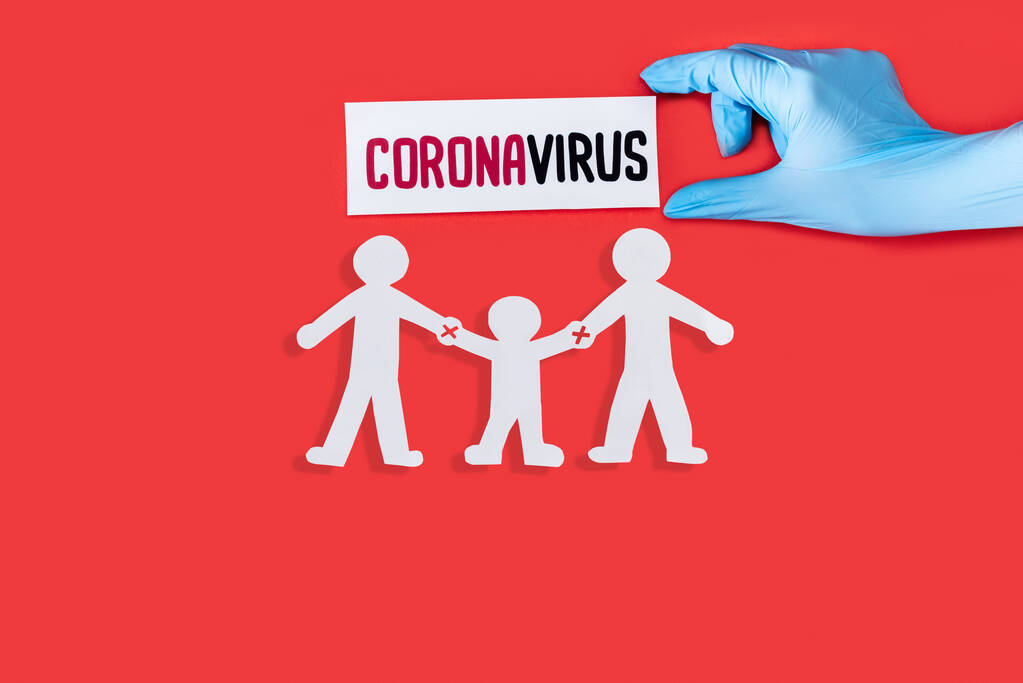 Doktorun üst görünümü lateks eldivenli elinde Coronavirus harfleri olan kırmızı üzerine izole edilmiş kağıttan insanlar.  - Fotoğraf, Görsel