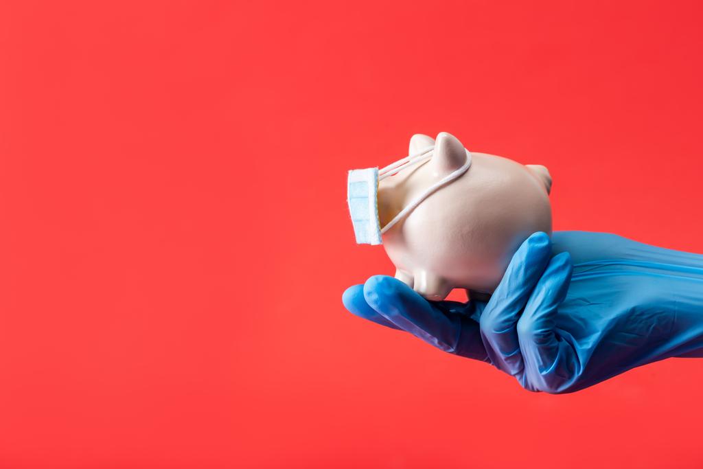 cropped view of doctor holding piggy bank in small medical mask isolated on red with copy space  - Photo, Image