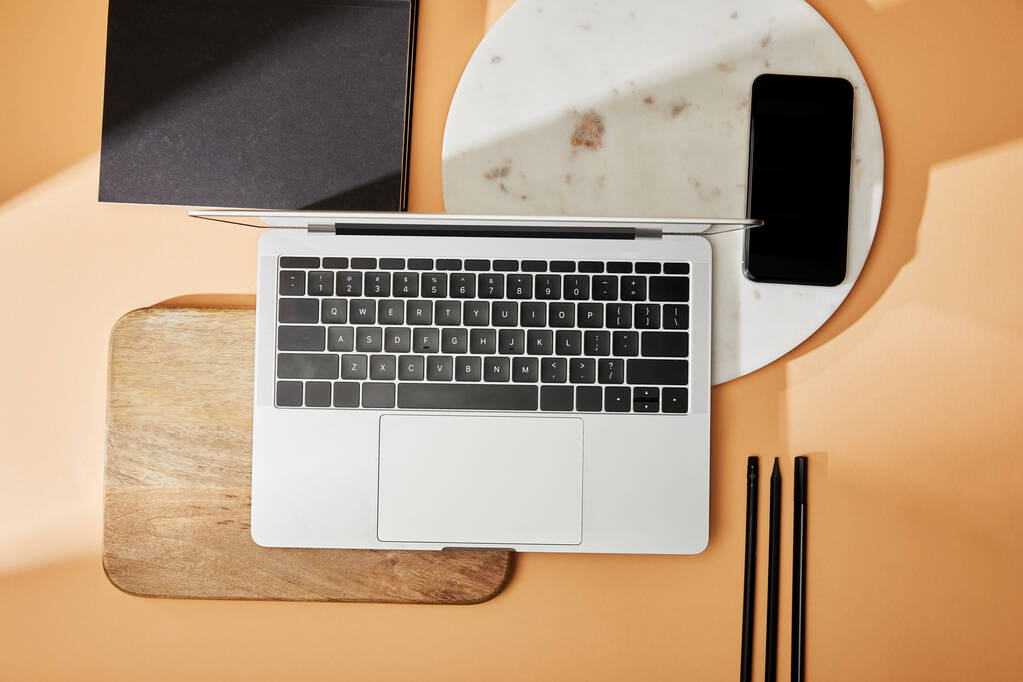 vue de dessus de l'ordinateur portable sur des planches en bois et en marbre, smartphone, pinceaux et cahiers sur fond beige
 - Photo, image