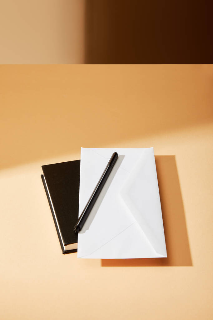 obálka, pero a černý zápisník na béžovém povrchu - Fotografie, Obrázek
